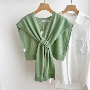 Close-up of green wool knit shawl with knot detail over a white shirt on wooden hanger