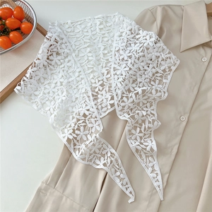 Detail of white lace floral shawl showing intricate hollow-out crochet texture on a beige shirt