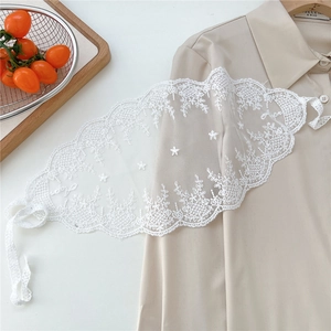 Detail showing white floral lace scarf with embroidery and ties on beige fabric background