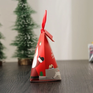 Pyramid-shaped red Christmas gift box with ribbon on wooden table among mini trees
