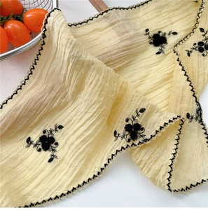 Detail of embroidered beige neck scarf with floral patterns and black wavy borders