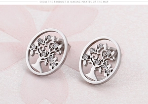 Close-up of silver Tree of Life stud earrings with crystals on a pink textured background