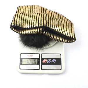 Detail shot of black and gold striped knit beanie weighing 101g on a digital scale