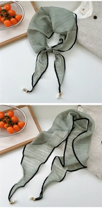 Detail of light green silk scarf with black piping edges and elegant pearl metal pendants