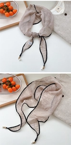 Detail of light coffee silk scarf with black piping and pearl pendants on white background