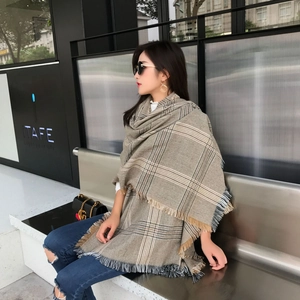 Detailed close-up of a large oversized khaki plaid scarf with fringe in a modern city setting
