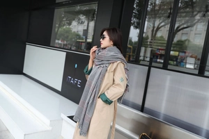 Detail of grey houndstooth scarf with tassels styled with a khaki trench coat for winter