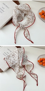 Dettaglio di un leggero foulard in cotone con motivo floreale e bordi rossi vivaci