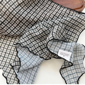 Detail of 100% polyester houndstooth scarf featuring decorative wavy ruffle edges