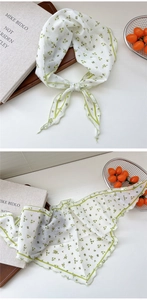 Close-up of floral print sheer neck scarf with green edge detailing on a wooden tray