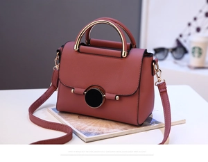 Close-up of pink lychee leather crossbody bag with golden ring hardware on a white desk