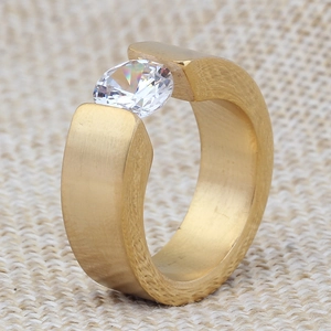 Detail view of gold tension set ring with a large white crystal on textured background
