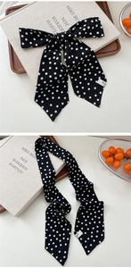 Close-up of black and white polka dot silk scarf tied in a bow on a wooden tray