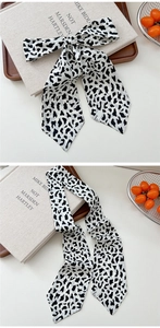 Detail of a black and white cow print skinny scarf tied in a bow on a white desk
