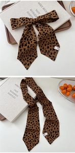 Detail view of leopard print silk scarf tied in a bow with a decorative woven label