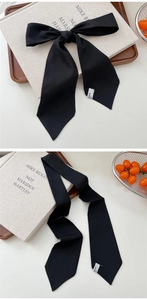 Detailed view of a black chiffon skinny scarf tied in a bow on a wooden tray