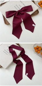 Detail of wine red silk scarf tied as a bow and laid flat on a minimalist table