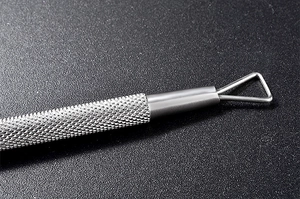 Vue macro d'un grattoir à ongles en acier inoxydable avec manche moleté et tête triangulaire