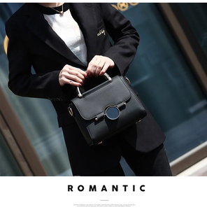 Detail of black pebbled leather handbag featuring circular metal lock and silver handle