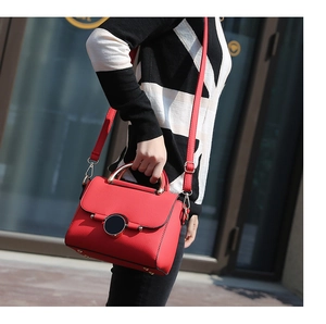 Detail of red lychee leather handbag featuring a circular magnetic clasp and metal handle