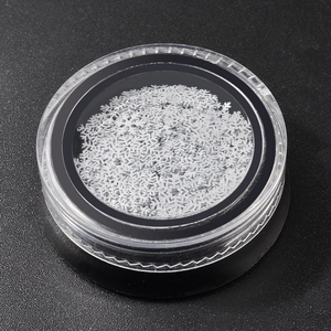 White snowflake nail art sequins in a clear round jar on a black background