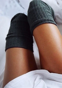 Detailed view of dark grey ribbed knit thigh-high socks on a soft white background
