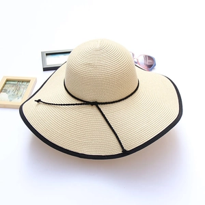Detail of beige straw sun hat with black trim and ribbon on white background