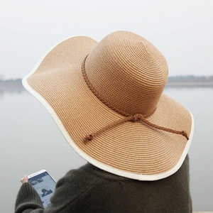 Rear view of a light brown wide-brimmed straw hat with white edge and woven ribbon