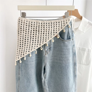 Detail view of beige crocheted cotton triangle scarf with fringe beads on blue jeans