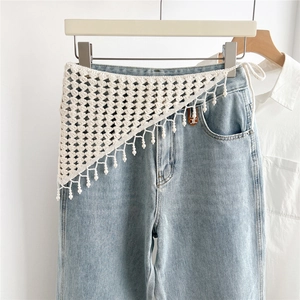 Close-up of white crochet triangle scarf with tassel fringe and beads on denim jeans