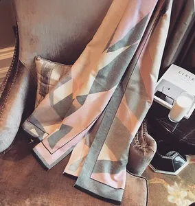 Detail view of thick geometric cashmere scarf in pink and grey over a velvet sofa