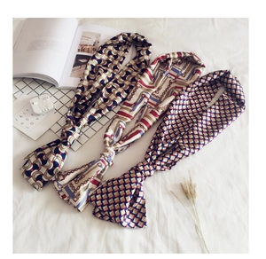Three elegant long silk scarves with geometric prints arranged on a soft white bed sheet