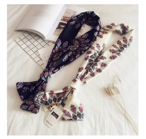 Close-up of bohemian paisley silk scarves on white bedding with decorative props