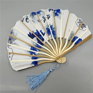 Close-up of white folding fan with blue floral patterns, bamboo ribs, and silk tassel