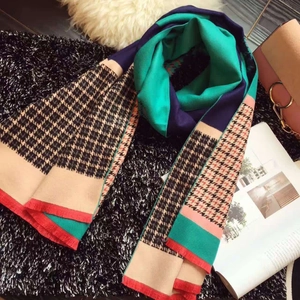 Flat lay of a thick houndstooth scarf with blue, green, and beige patchwork and orange fringe