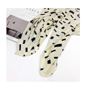 Macro detail of a beige cotton-linen scarf with black geometric patterns and soft texture