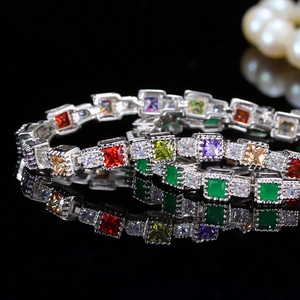 Elegant silver tennis bracelets with colorful square zircons on a black reflective surface