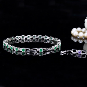 Detail of silver bracelet with green square stones and clear crystals on a black surface