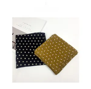 Close-up of navy and yellow patterned square silk scarves folded on a white table