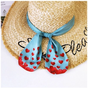 Detail of beige straw sun hat with black embroidery and heart-printed blue ribbon bow