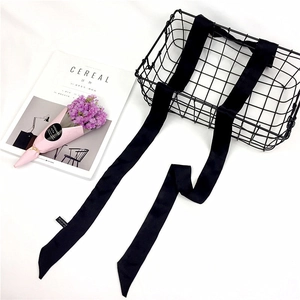 Detail view of a long black satin skinny scarf draped over a black wire basket with decor