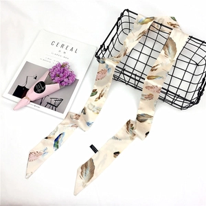 Detail of a narrow cream silk scarf with colorful feather prints inside a black wire basket