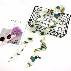 Detail of silk-like skinny scarf with parrot and leaf print draped on a metal basket
