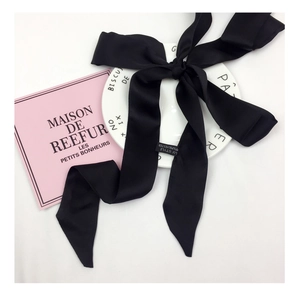 Detail of elegant black polyester satin skinny scarf tied in a bow on a white ceramic plate