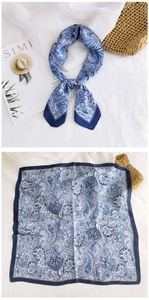 Detailed blue paisley silk scarf showing tied knot and flat layout on white textured background