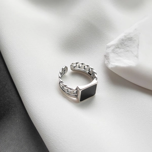 Macro detail of silver vintage chain ring featuring a black square inlay on silk background