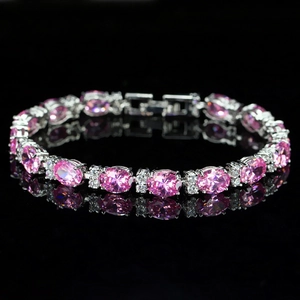 Macro shot of silver tennis bracelet with oval pink gemstones on a black mirror surface
