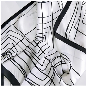 Detailed view of the smooth silk texture and black geometric line pattern on a white scarf
