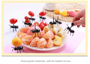 Creative black ant-shaped fruit forks holding sliced fruits on a white tray