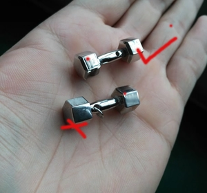 Close-up of silver hexagon dumbbell steel earrings held in palm for scale